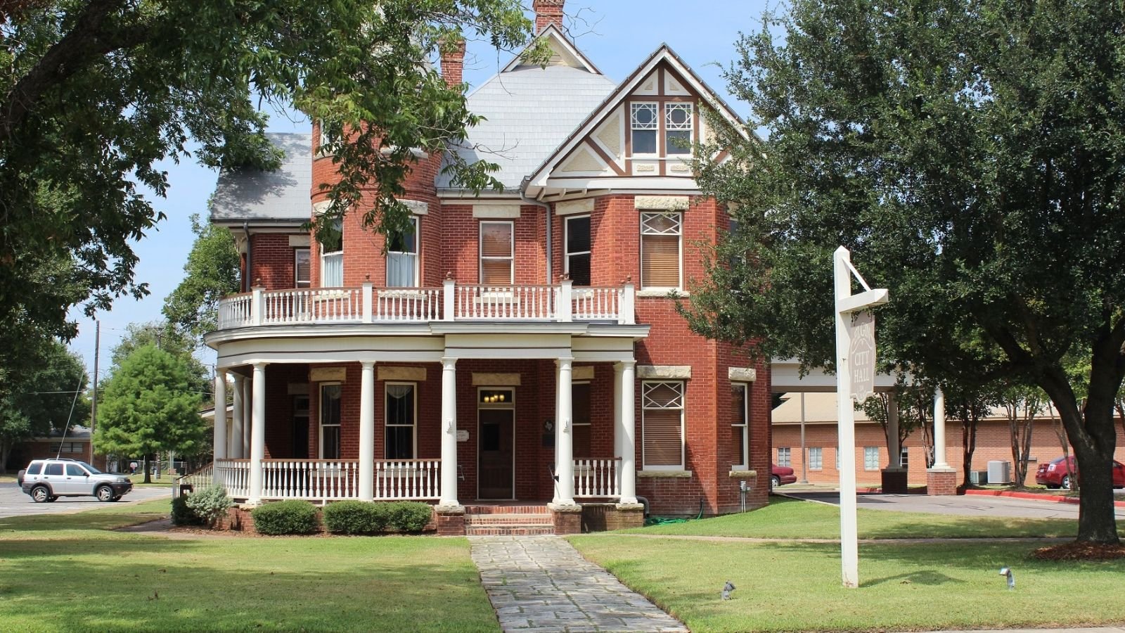 Historic red brick Elgin City Hall building with a wraparound porch in Elgin, Texas